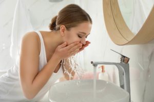 Young woman washing her face at the sink