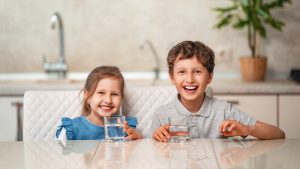 A young boy and girl smiling happily, holding a glass of clean water