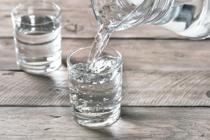 Close view of someone pouring water into a glass on a wooden table.